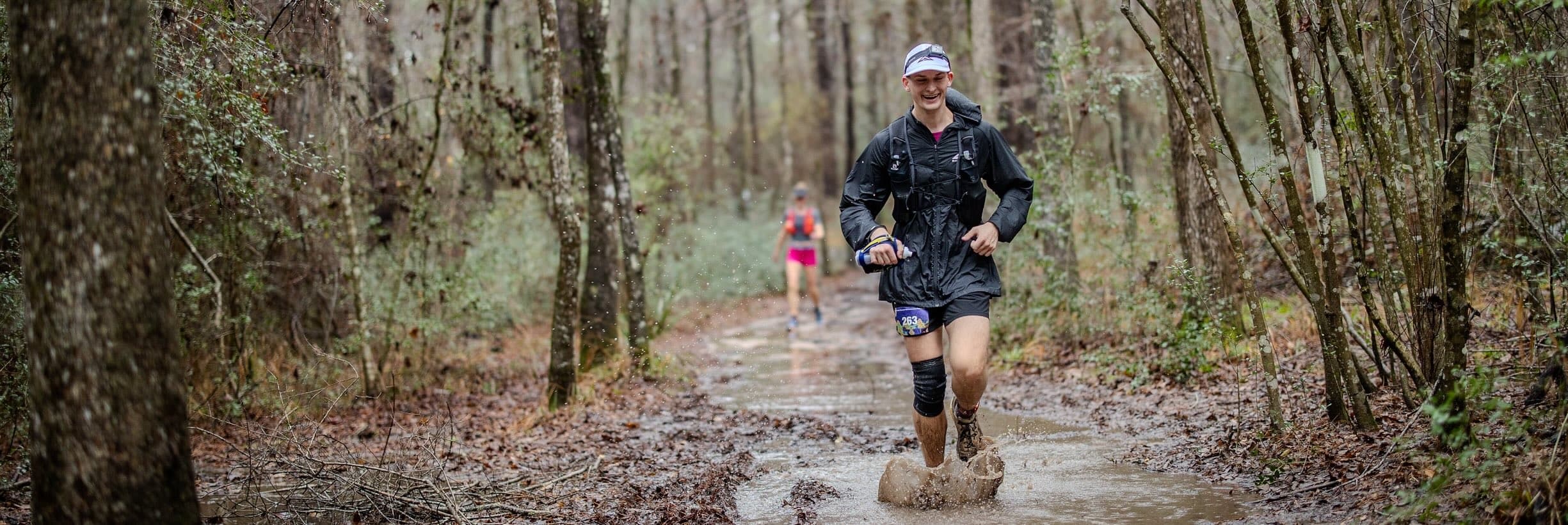 A long distance marathon runner, jogging along a wooded trail.